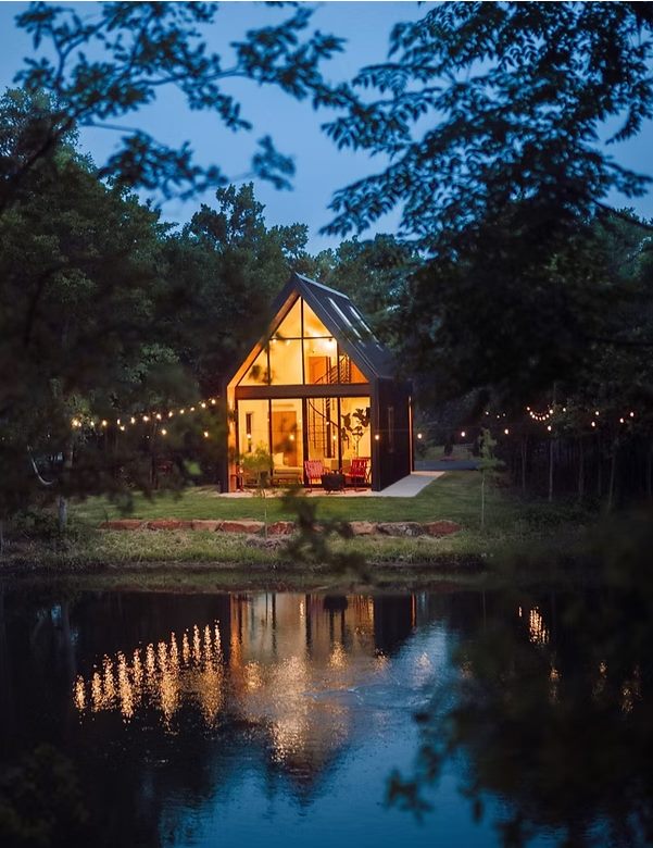 Glass-fronted modular cabin lit at dusk beside a lake, used as concept imagery